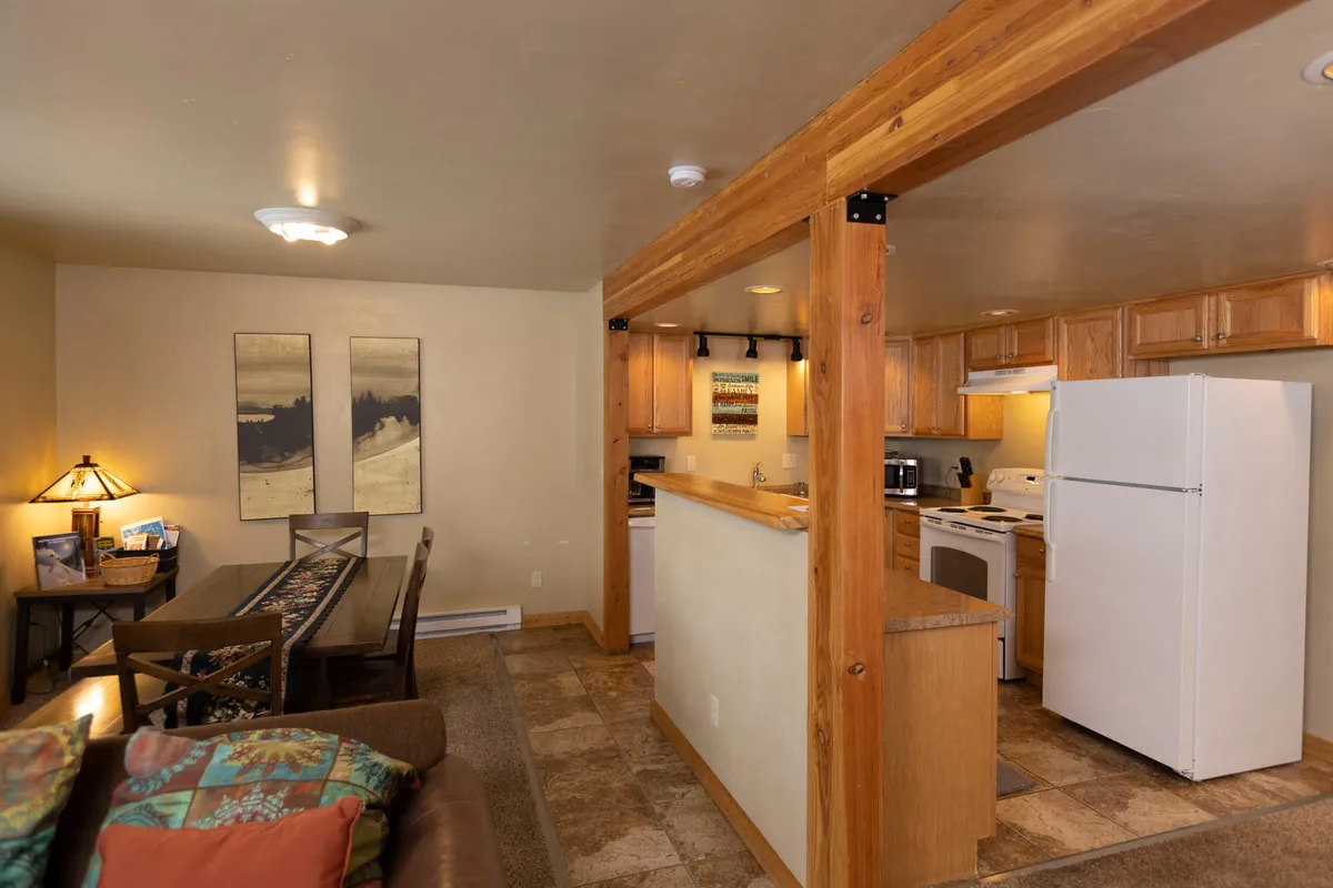 A bright dining area seamlessly connected to a modern kitchen and a living space with a cozy sofa and colorful pillows. The scene captures a relaxed, lived-in atmosphere, ideal for casual gatherings and sharing homemade meals.