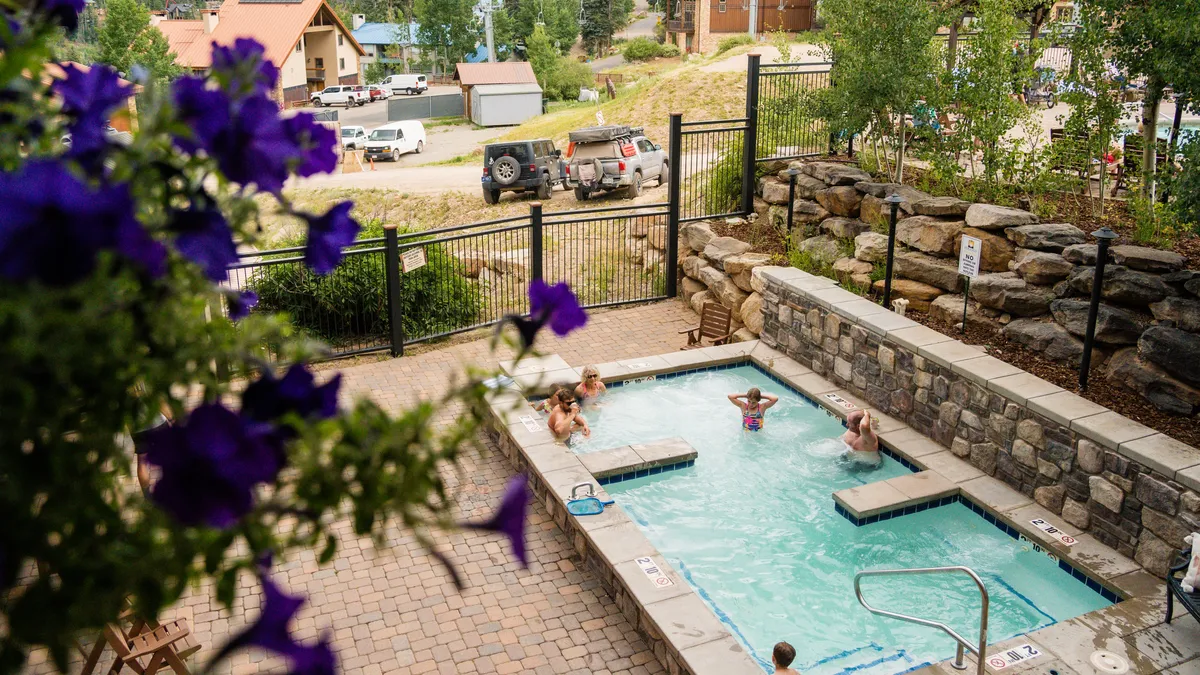 An inviting spa pool surrounded by blooming flowers and a natural rock wall, with open sky above. The area exudes relaxation and offers a glimpse of the mountains in the distance, suggesting a tranquil retreat after outdoor adventures.