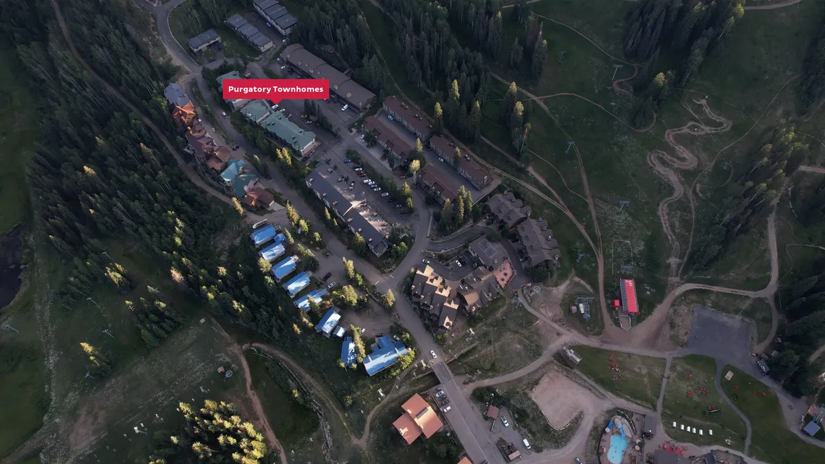 An inviting exterior scene of Purgatory Townhomes nestled among a vibrant green forest, with winding paths leading toward nearby recreational areas. The backdrop showcases sunset views over the mountains, and the overall atmosphere feels welcoming and adventurous, with hints of wildlife and stargazing opportunities.