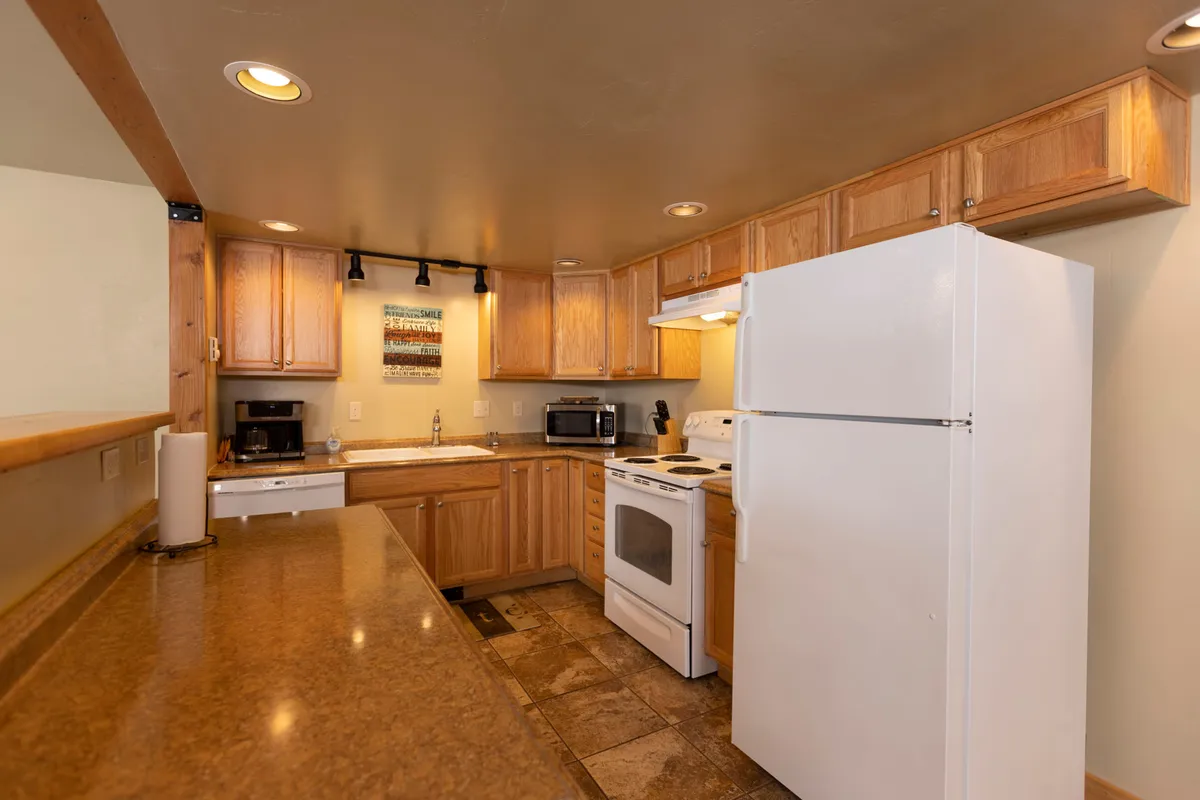 A spacious, well-equipped kitchen featuring an inviting kitchen counter, stainless steel refrigerator, modern stove, and warm wood cabinetry. The layout suggests room for both cooking and socializing, with plenty of workspace for preparing meals and gathering.