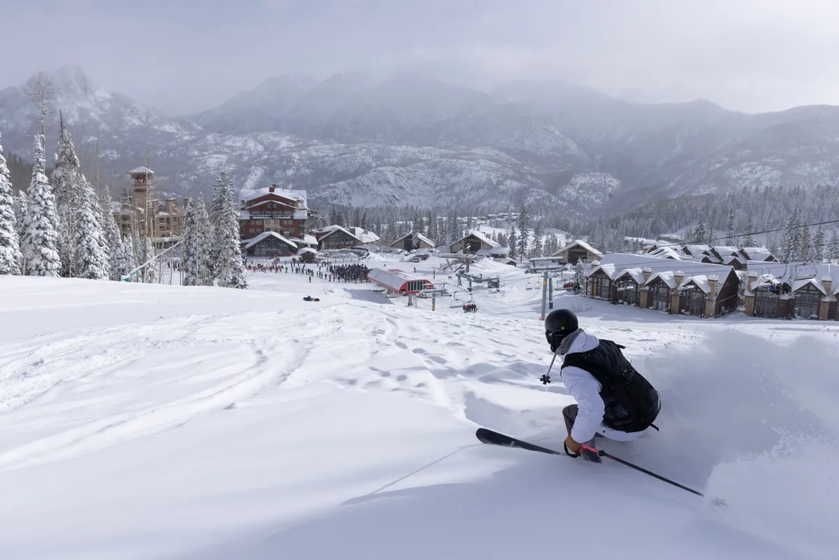 A skier is captured in motion amidst the snow-covered mountains at Purgatory Resort, with the ski lift, resort buildings, and breathtaking wintry landscape clearly visible. The image radiates the thrill and energy of a day spent on the slopes.