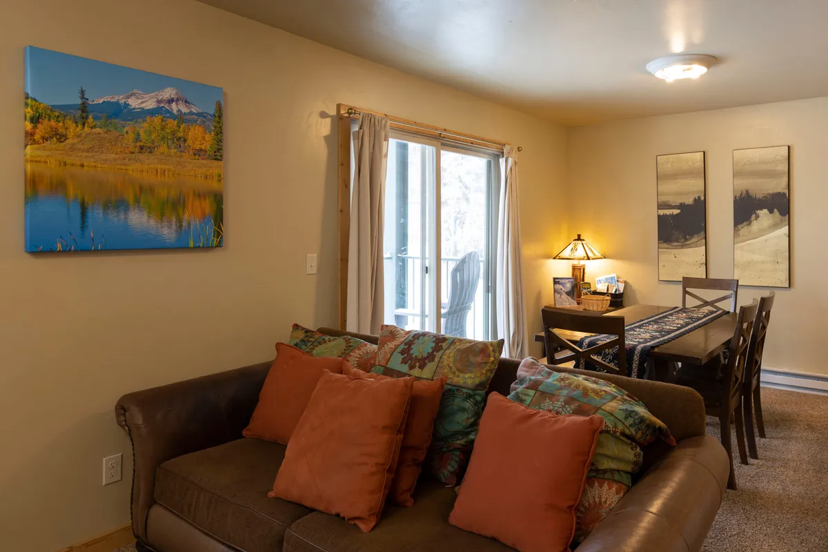 A cozy and colorful living area with a comfortable couch, a dining table positioned to enjoy views of the outdoors, and vibrant artwork on the wall. The space is filled with natural light, suggesting a welcoming environment for families and groups.