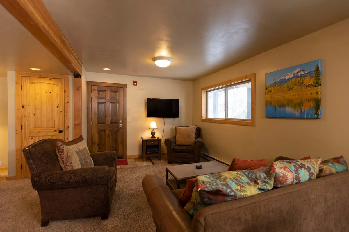 The image highlights a comfortable seating area with a sofa, wooden door, television, and landscape artwork. Natural light fills the room, creating a warm and inviting atmosphere for group activities like movie nights, games, or simply relaxing together.