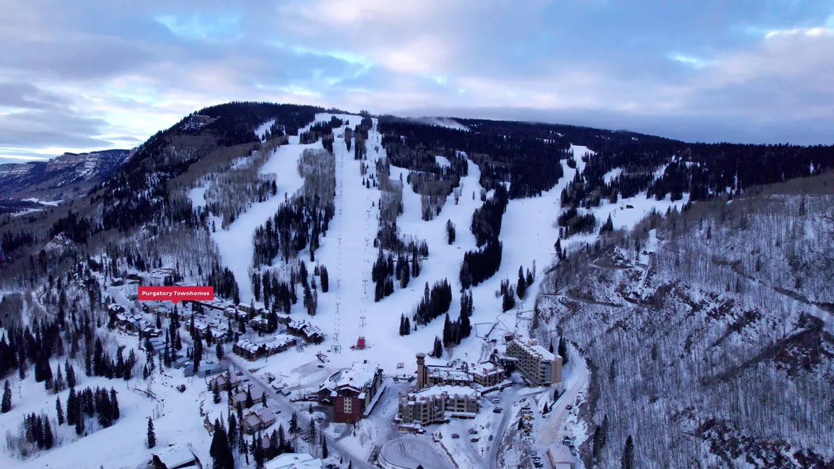 A dynamic exterior image showing ski slopes, townhouses, ski lifts, and a breathtaking mountain range. The scene is alive with activity, suggesting opportunities for skiing, snowboarding, and hiking, all just moments from the homes themselves. The mood is adventurous, with the town nestled cozily amidst the landscape.