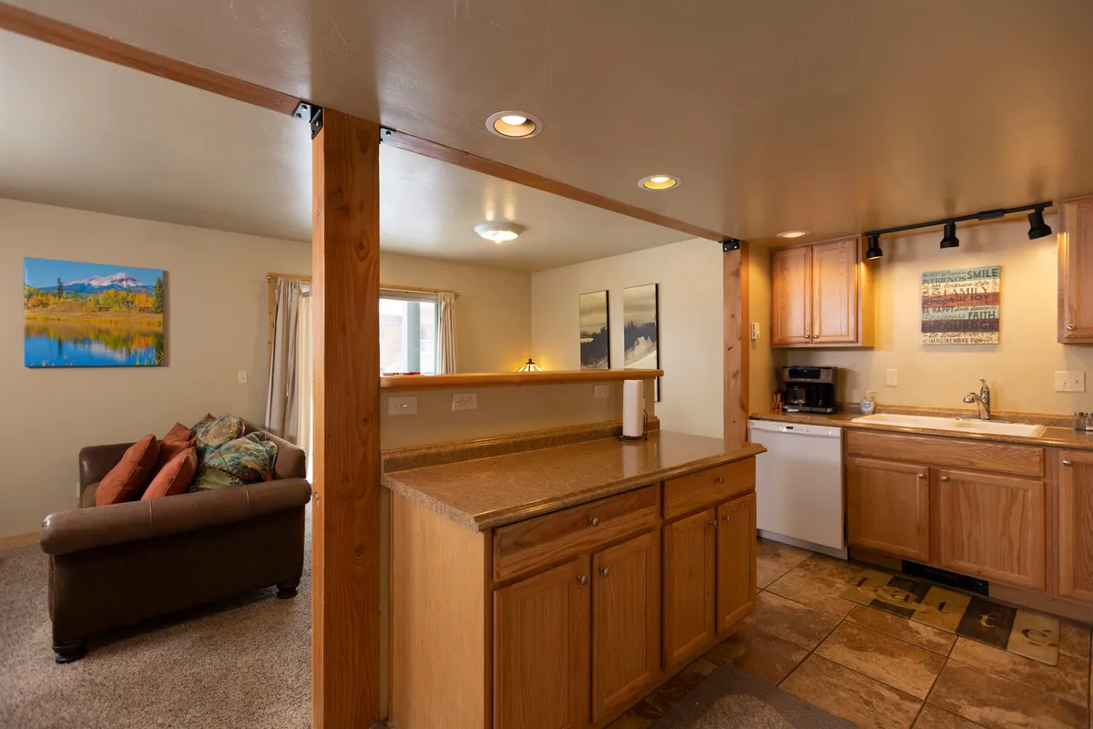 An open-plan kitchen and living room area that highlights ample seating and a welcoming atmosphere, with artwork providing a touch of local inspiration. The setup is ideal for group relaxation after a day of alpine adventures, and the visible countertop hints at shared meals and socializing.